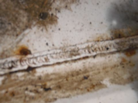 1993 Ford Bronco - Close-up of a welded seam on a dirty white surface, showing signs of rust and wear.