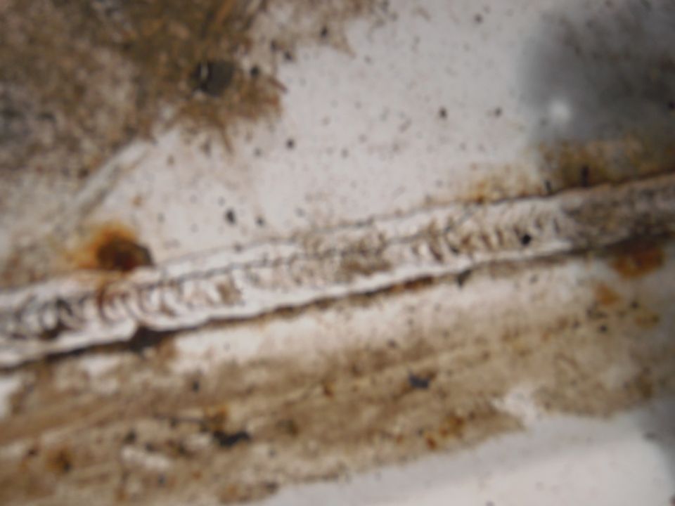 Welded seam on dirty white surface with rust spots