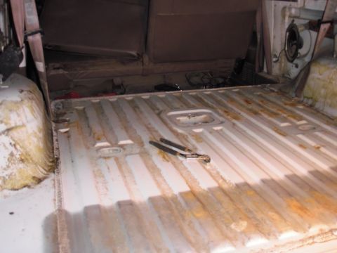 1993 Ford Bronco - The interior cargo area of a vehicle shows a ribbed floor with rust stains and brown seats, with a pair of pliers on the floor.