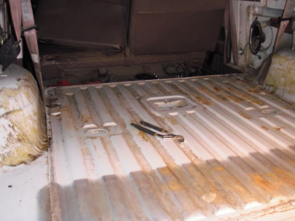 White interior cargo area with ribbed floor, rust stains, and brown seats. Pliers rest on the floor