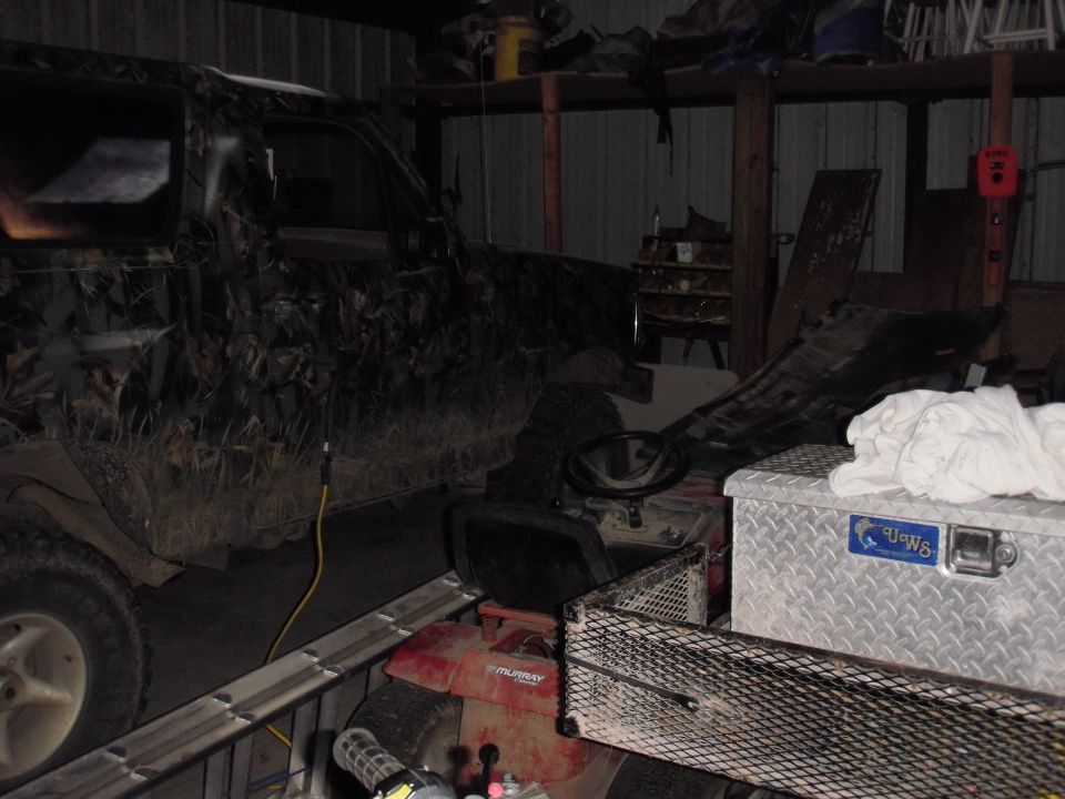 Camouflaged SUV parked next to a riding mower and a toolbox in a garage