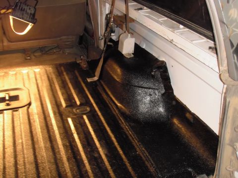 1993 Ford Bronco - The interior of a vehicle shows a freshly applied black bedliner coating on the rear wheel well and floor.