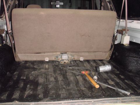 1993 Ford Bronco - Tools are laid out in the bed of a truck, near a folded-up brown bench seat.