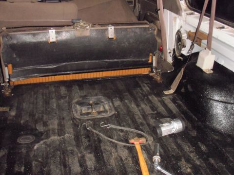 1993 Ford Bronco - The interior of a vehicle, likely a Ford Bronco, shows the rear floor area with a seat folded up. Tools including a hammer, wrench, and fla…