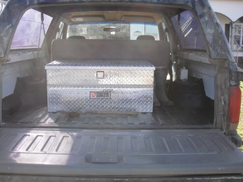 1993 Ford Bronco - View through the open tailgate into the spray-lined cargo area of a full-size SUV, with a diamond-plate aluminum Tractor Supply Co. toolbox…