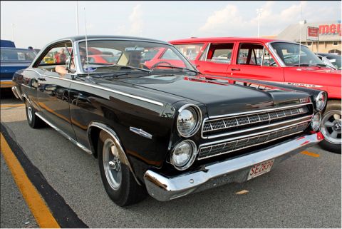 1966 Mercury Comet - A black 1966 Mercury Comet coupe is parked next to a red station wagon, with a store in the background.