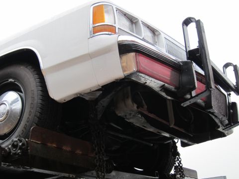 1991 Ford Crown Victoria LTD - The rear of a white sedan is visible, secured with chains on a trailer.