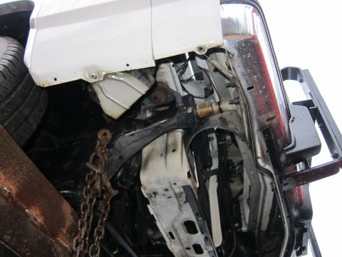 1991 Ford LTD Crown Victoria - Underside view of a white vehicle's suspension and chassis, showing a chain attached to the frame.
