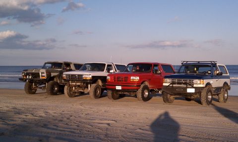 1979 Ford Bronco - A group of four-wheel-drive vehicles are lined up on the sand near the ocean.