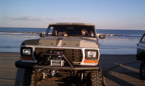 1979 Ford Bronco - A 1979 Ford Bronco with camouflage paint sits on a sandy beach with the ocean in the background.
