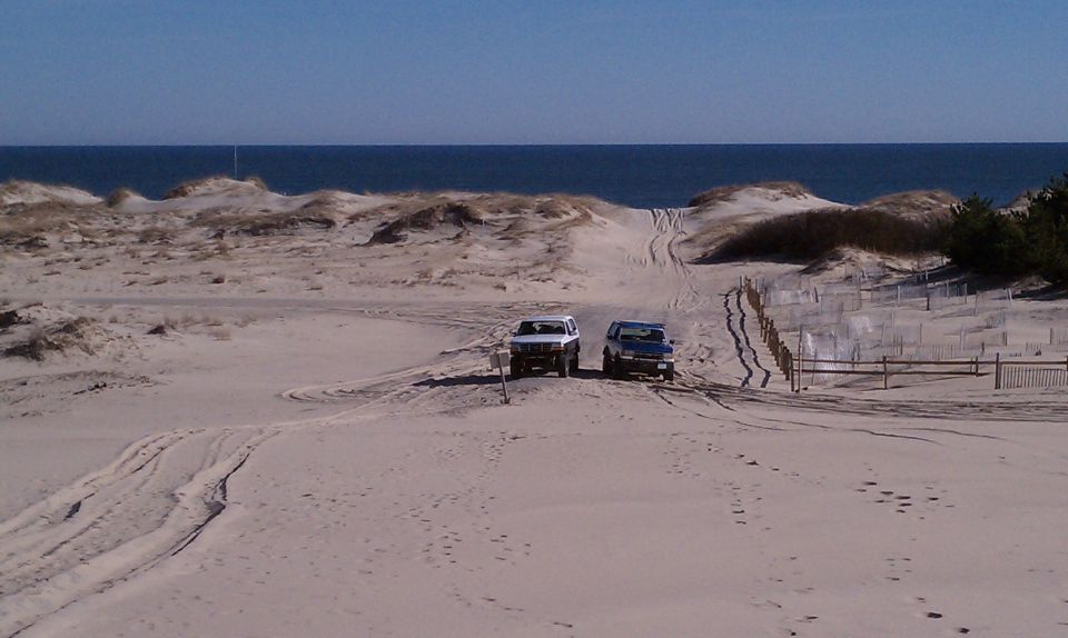 Two SUVs on a sandy beach with dunes and the ocean in the background