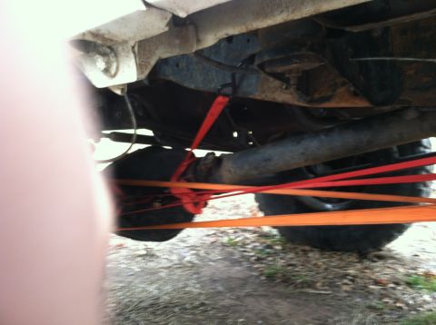 1996 Ford Bronco - Straps secure the rear axle and tire of a vehicle, revealing its rusty undercarriage.