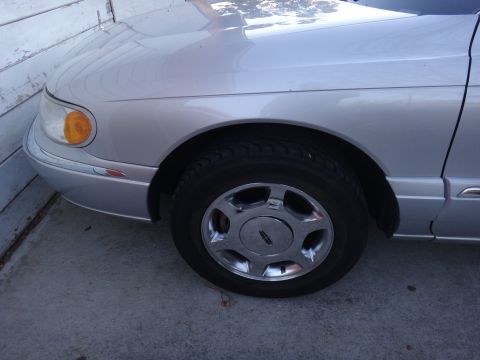 2000 Lincoln Continental - The front fender and wheel of a silver sedan, identified by the Lincoln logo on the hubcap, suggest a model year around 1998.