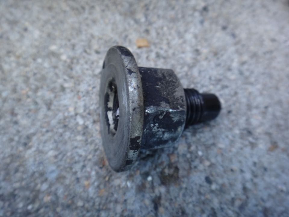 Motor mount bolt with a washer and threaded end, resting on a concrete surface