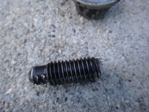 2003 Ford Taurus - A close-up view of a stripped bolt and a portion of a motor mount resting on a concrete surface.
