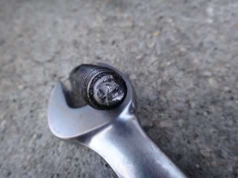 2003 Ford Taurus - A close-up view of a damaged bolt head being held by a metal wrench against a concrete surface.