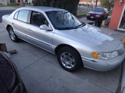 2000 Lincoln Continental - A silver sedan is parked on a concrete driveway next to a building.