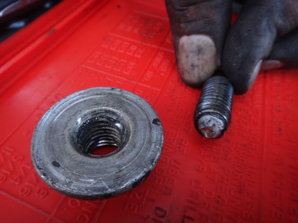 Close-up of a used motor mount bolt and nut on a red tray