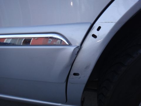 2000 Lincoln Continental - Damage to the rear quarter panel of a silver vehicle, with a chrome trim piece visible.