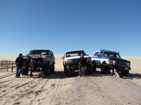 1979 Ford Bronco - A group poses with their off-road vehicles on a sunny day at the beach.