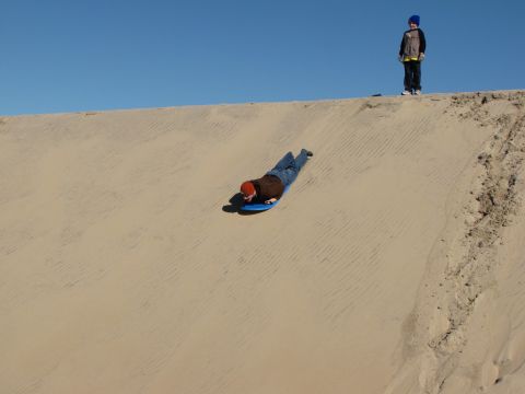 1979 Ford Bronco - Two children enjoy a sunny day sledding down a large sand dune.