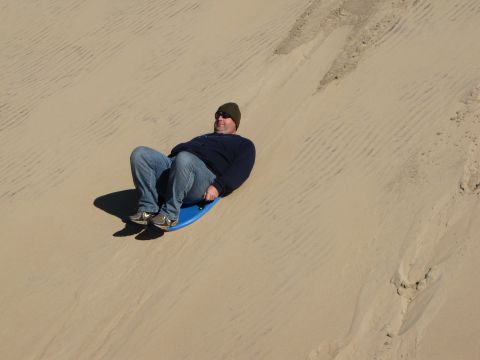 1979 Ford Bronco - A man enjoys a ride down a sand dune on a blue sled.