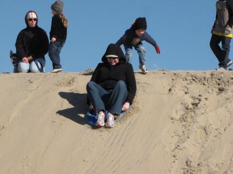 1979 Ford Bronco - Several people are enjoying a day of sledding down large sand dunes.