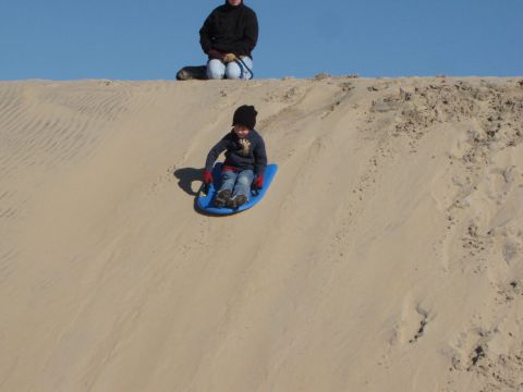 1979 Ford Bronco - A child enjoys a ride down a sandy slope on a blue sled, while an adult observes from above.