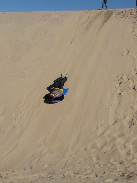 1979 Ford Bronco - A person slides down a sandy slope on a blue mat, with other people visible at the top of the dune.