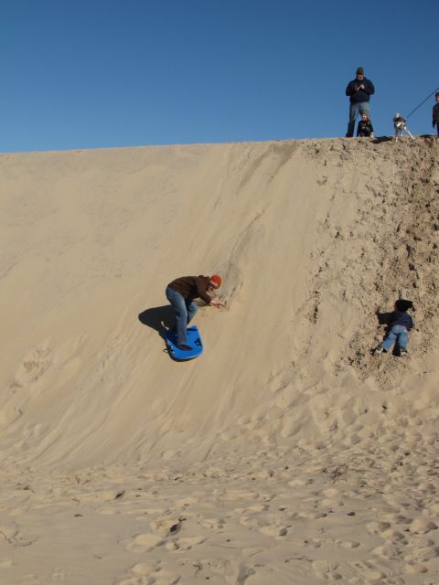 1979 Ford Bronco - People enjoy sandboarding down a large sand dune on a clear day.