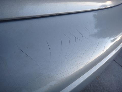2000 Lincoln Continental - Close-up of cracked paint on a silver car bumper, indicating wear and tear.