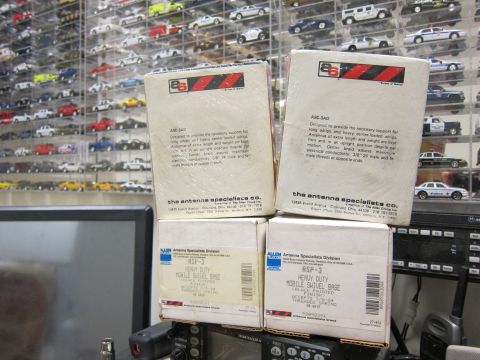 1991 Ford LTD Crown Victoria - Several boxes of antenna parts are stacked, with radio equipment below and a collection of model cars displayed behind.
