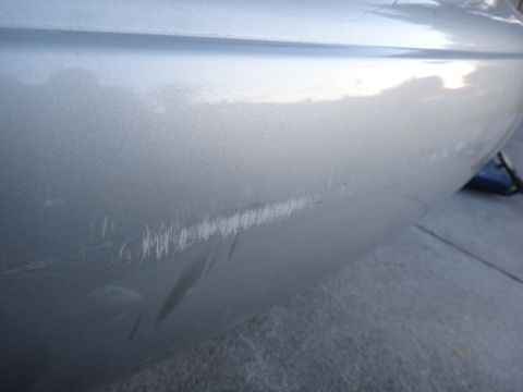 2000 Lincoln Continental - A close-up view of a silver car's rear bumper reveals extensive damage from scratches.