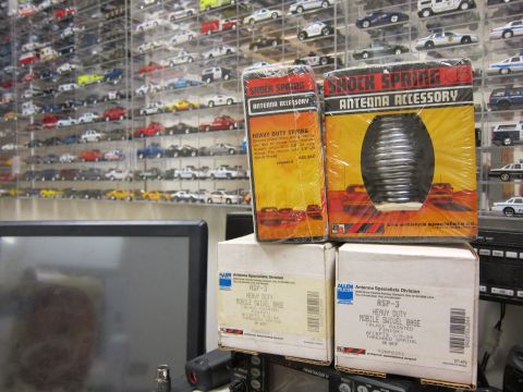 1991 Ford LTD Crown Victoria - Boxes of antenna accessories, including a shock spring, are displayed in front of a wall of model cars.