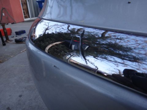 2000 Lincoln Continental - Close-up of a car's rear bumper chrome trim, reflecting the surrounding environment.