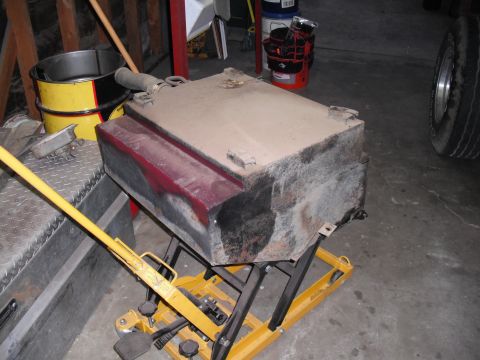 1968 Ford Bronco - A dusty fuel tank is positioned on a yellow lift, with a tire visible in the background.