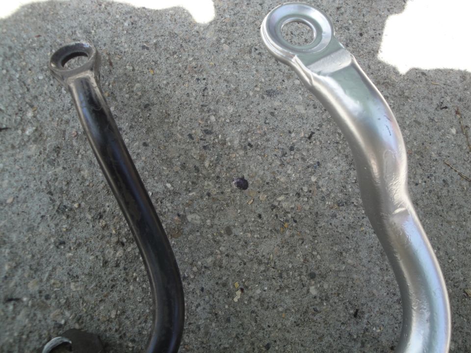 Two sway bar end links, one black and one silver, on a concrete surface