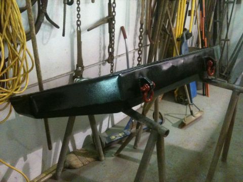 1996 Ford Bronco - Aftermarket front bumper with tow hooks is painted and drying on sawhorses in a garage.