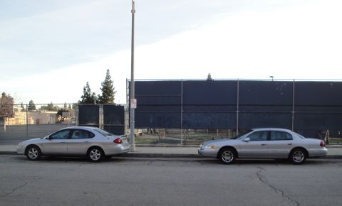 2000 Lincoln Continental - Two silver sedans are parked side-by-side on a street with a dark fence in the background.