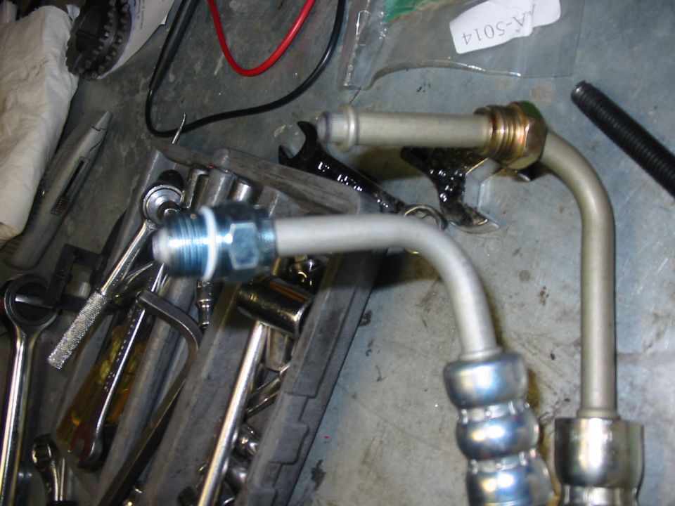 Two metal power steering lines with fittings and blue O-rings, resting on a toolbox with wrenches