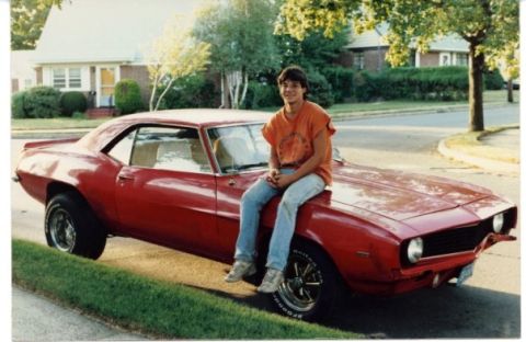 2005 Ford Excursion - A young man poses on the hood of a classic red Chevrolet Camaro parked curbside in front of a suburban house.