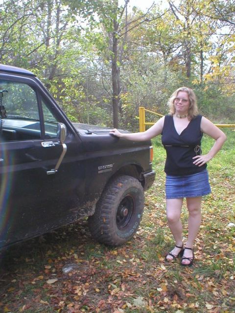 1989 Ford Bronco - Driver's-side profile of a dark blue Ford truck on a grassy, leaf-covered trail, showing the door with chrome handle, black side mirror, fe…