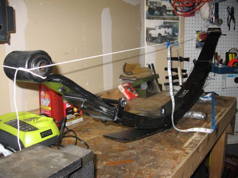 1995 Ford Bronco - Leaf spring assembly with part number 23411 visible, on a workbench with tools and a charger.