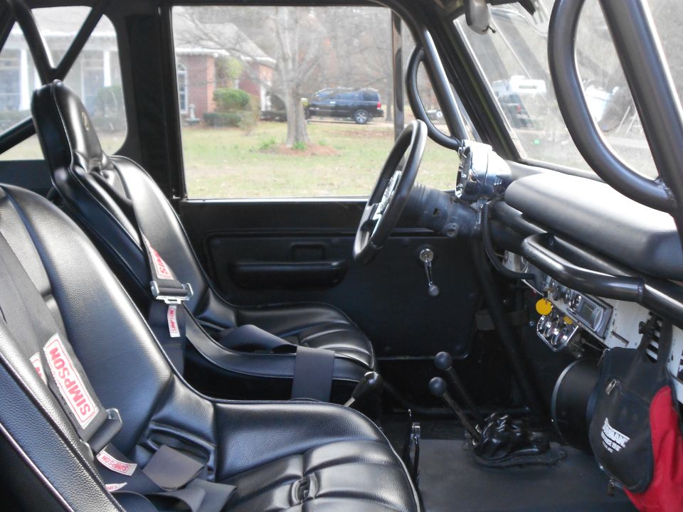 Vintage 4x4 interior with black bucket seats, Simpson harnesses, roll cage and floor shifters