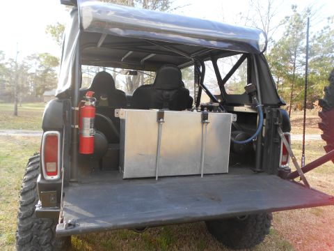 1967 Ford Mustang - Rear view of an early Ford Bronco with the tailgate down and soft top up, showing the interior with black bucket seats, a roll bar, a red f…