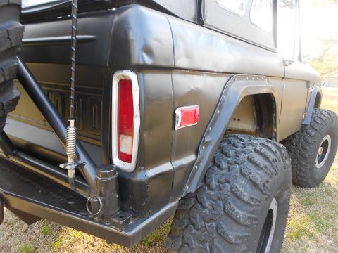 1967 Ford Mustang - Rear driver-side quarter of a first-generation Ford Bronco painted flat black, showing the vertical taillight, 'FORD' embossed tailgate let…