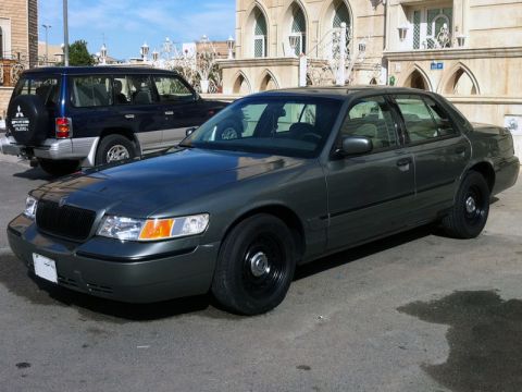 2001 Mercury Grand Marquis - A dark gray sedan is parked on a street in front of a building, with another vehicle behind it.