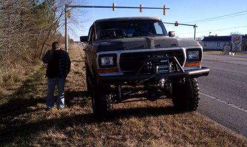 1979 Ford Bronco - A person stands next to a lifted 1979 Ford Bronco on the side of a road with a Burger King in the background.
