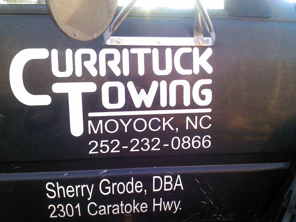 Side of a dark vehicle with white text: CURRITUCK TOWING, MOYOCK, NC, 252-232-0866, and Sherry Grode, DBA, 2301 Caratoke Hwy