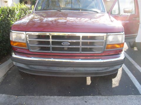1995 Ford F-150 - The front grille and headlights of a red Ford F-150 are visible, with the driver's side door open.